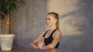 Female coach yoga makes namaste gesture by hands indoors in the morning