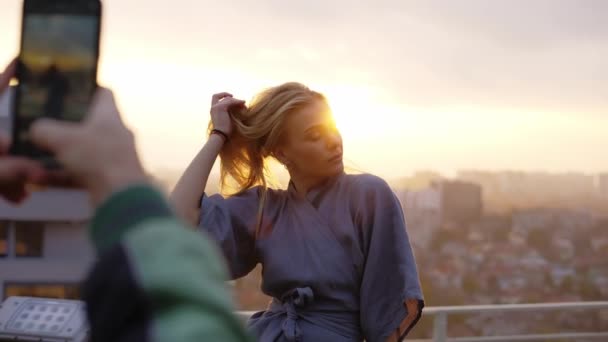 Sexy blonde in robe stands on terrace and poses for a photo, touching her hair