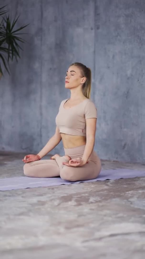 Young female sitting in Lotus Pose or Padmasana with closed eyes and holding her hands in Gyan Mudra making deep breath — Stockvideo
