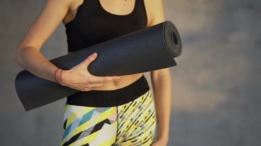 Close up overview of a woman athlete posing with mat in hand standing in loft room