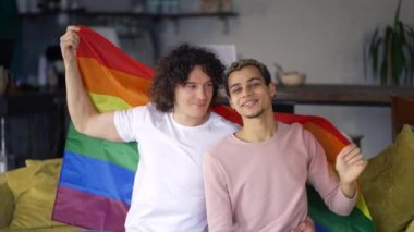 Guys spend time together at home on the couch under lgbt colorful rainbow flag