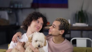 Lovely homosexual male gay couple in love enjoying time together while stroking the dog on sofa