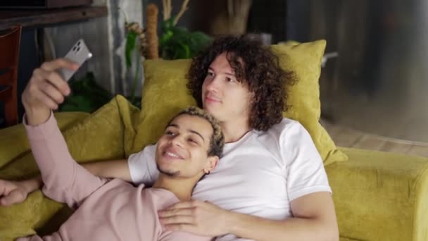 Male romantic gay couple relaxing on the couch, taking selfie with smartphone, posing — Vídeo de Stock