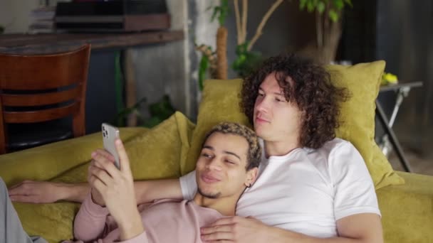 Male romantic gay couple relaxing on the couch, whatching the smartphone screen — Stock Video
