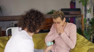 Genç bir adam erkek arkadaşına evlenme teklif ediyor. Oturma odasında bir kanepede kucaklaşıyor.