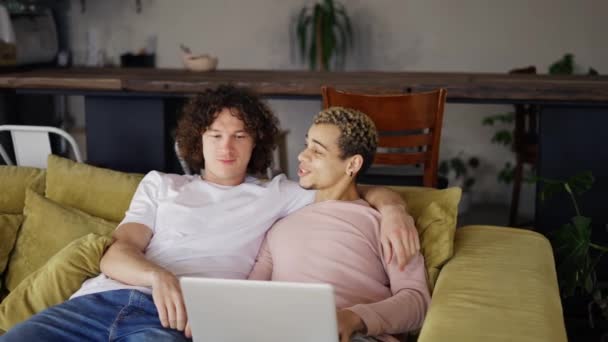 Όμορφο γκέι ζευγάρι που χρησιμοποιεί φορητό υπολογιστή, ενώ κάθεται σε ένα σαλόνι σε άνετο κομψό διαμέρισμα — Αρχείο Βίντεο