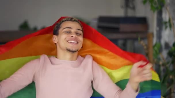 Curly bonito homem segurando bandeira do arco-íris em casa — Vídeo de Stock