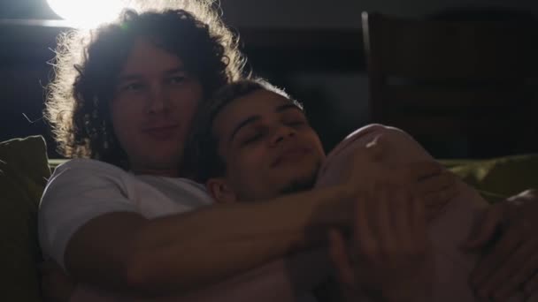 Lockdown de joven pareja gay en abrazo en sofá en sala de estar, descansando y viendo películas — Vídeo de stock