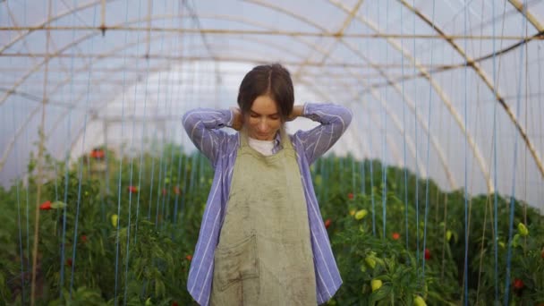 Junge Gärtnerin zieht Schürze an, bereit für Arbeit im Gewächshaus des Pflanzengeschäfts — Stockvideo