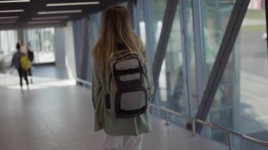 Havaalanı terminalinde sırt çantası taşıyan kadın turistin arka görüntüsü.