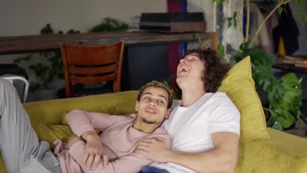 Joven gay macho pareja relajarse en sofá abrazando tener divertido — Vídeo de stock
