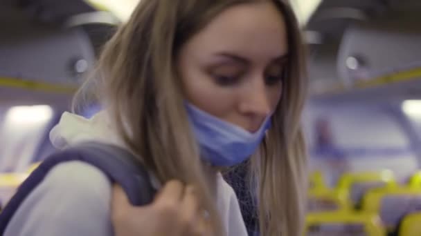 Piękna dziewczyna w masce z plecakiem w samolocie przechodzi korytarzem — Wideo stockowe