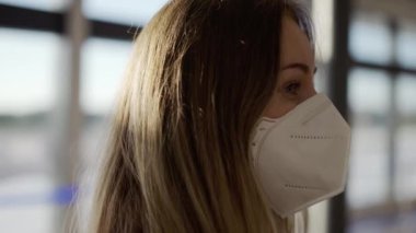 Havaalanında duran koruyucu maskeli, kafası karışık bir kadın.