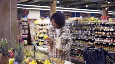 Afro-Amerikalı bir kadın süpermarketten portakalları kağıt torbaya koyuyor.