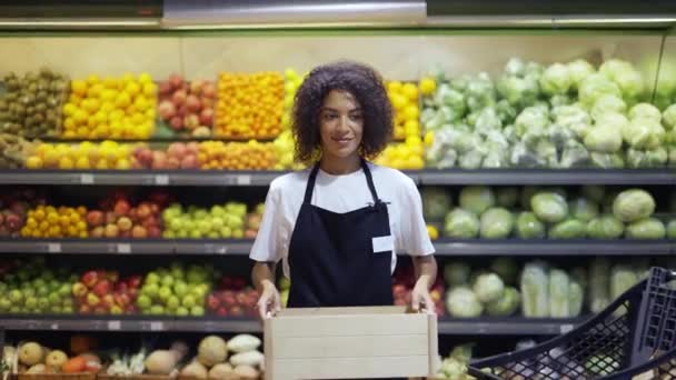 Krásná usmívající se mladá žena supermarket zaměstnanec v černé zástěře drží krabici — Stock video