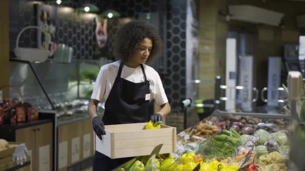 Мультирасовый работник в черном фартуке кладет желтый перец в супермаркет — стоковое видео