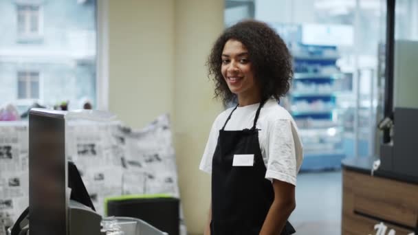 Retrato de un trabajador afroamericano en la caja de la tienda de comestibles, sonriendo amigablemente a la cámara — Vídeos de Stock