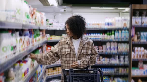 Femme noire positive avec appareil mobile et chariot achetant des produits au centre commercial — Video