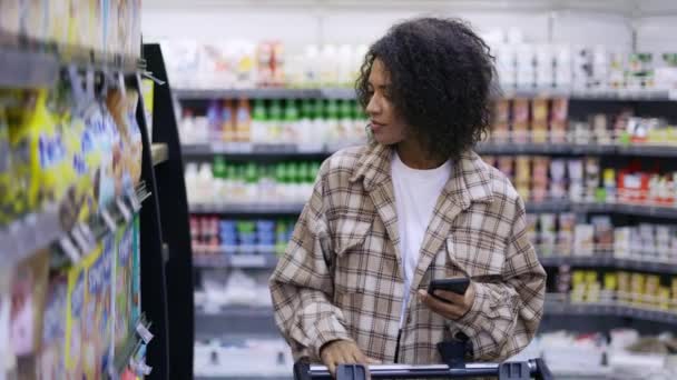 Афроамериканец с корзиной с использованием смартфона в супермаркете, замедленная съемка — стоковое видео
