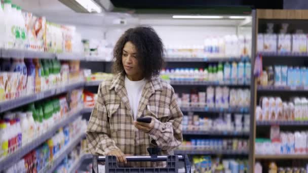 Afroamerykanka sprawdzanie listy zakupów na smartfonie w supermarkecie — Wideo stockowe