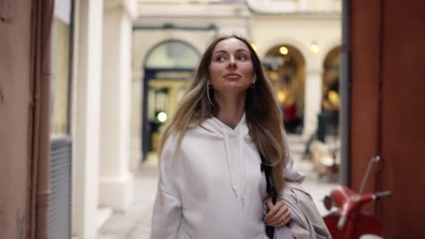 Жінка гуляє по міській вузькій вулиці з рюкзаком, виглядає з цікавістю навколо — стокове відео