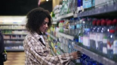 Siyah kadın süpermarkette alışveriş yapıyor, su şişeleri arıyor.