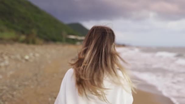 Retrato retrovisor de una mujer rubia caminando por la costa del océano, hablando por teléfono — Vídeos de Stock