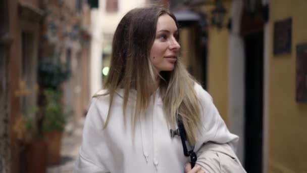 Attraktiv kvinna promenader längs en stad smal gata med ryggsäck, ser med intresse runt — Stockvideo