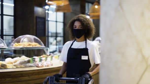 Africké americké pracovnice tlačí vozík v supermarketu, nosí ochrannou masku — Stock video