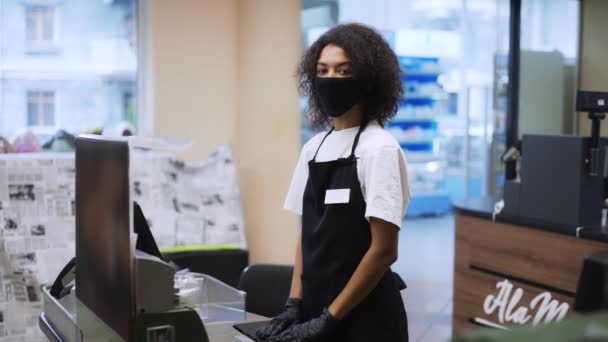 Egy afro-amerikai munkás portréja egy élelmiszerbolt pénztáránál, maszkban. — Stock videók
