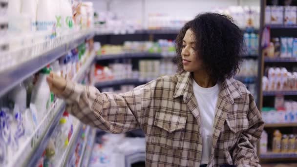 Черная женщина делает покупки в супермаркете, смотрит на полки с едой — стоковое видео