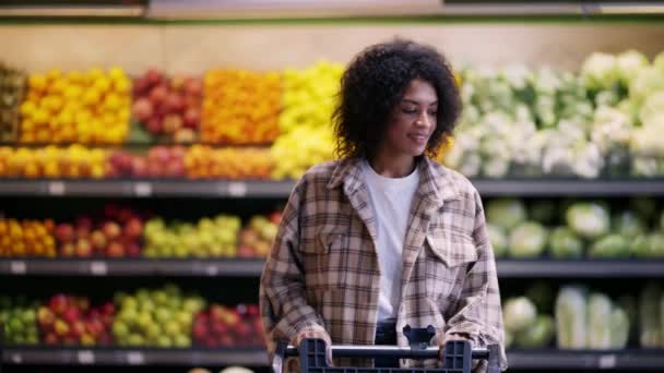 Femme gaie marche à travers le supermarché avec chariot, prendre un paquet de pommes de terre — Video