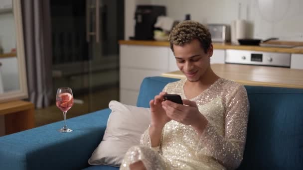 Relaxante transexual cara em vestido fantasia em um sofá usando telefone celular — Vídeo de Stock