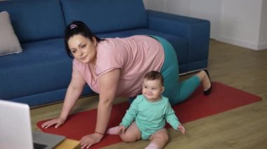 Aşırı kilolu bir kadın yanında küçük bir bebekle internetten egzersiz yapıyor.