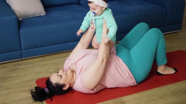 Plump mor holder en buttet smilende baby i armene hjemme på gulvet – Stock-video