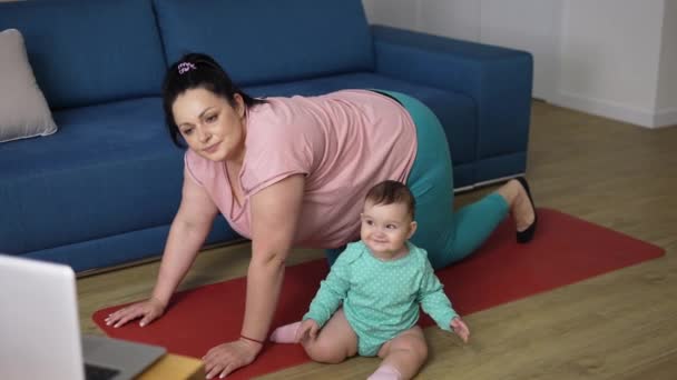 Übergewichtige Frau macht online vom Laptop aus Übungen mit kleinem Baby neben sich — Stockvideo