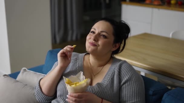 Grande taille femme mange des frites avec beaucoup de plaisir assis sur un canapé — Video