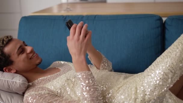 Fröhlicher Kerl in Verkleidung mit Handy auf Sofa liegend — Stockvideo