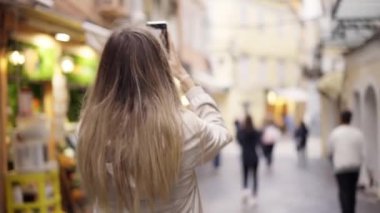 Eski şehirdeki mutlu beyaz kadın modern akıllı telefondan fotoğraf çekiyor.