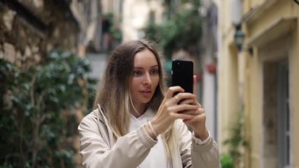 旧市街の幸せな白人女性が関心を持って現代のスマートフォンで写真を撮る — ストック動画