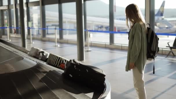Ταξιδιωτική γυναίκα περιμένει στο αεροδρόμιο δίπλα σε ιμάντες μεταφοράς αποσκευών — Αρχείο Βίντεο