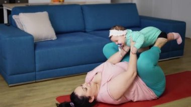 Genç bir annenin vücudunun kilo kaybı. Çocuklu kadın paspasın üstünde egzersiz yapıyor.