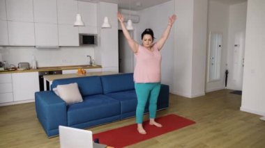 Tombul kadın dizüstü bilgisayarında öğretmeniyle evde yoga yapıyor.