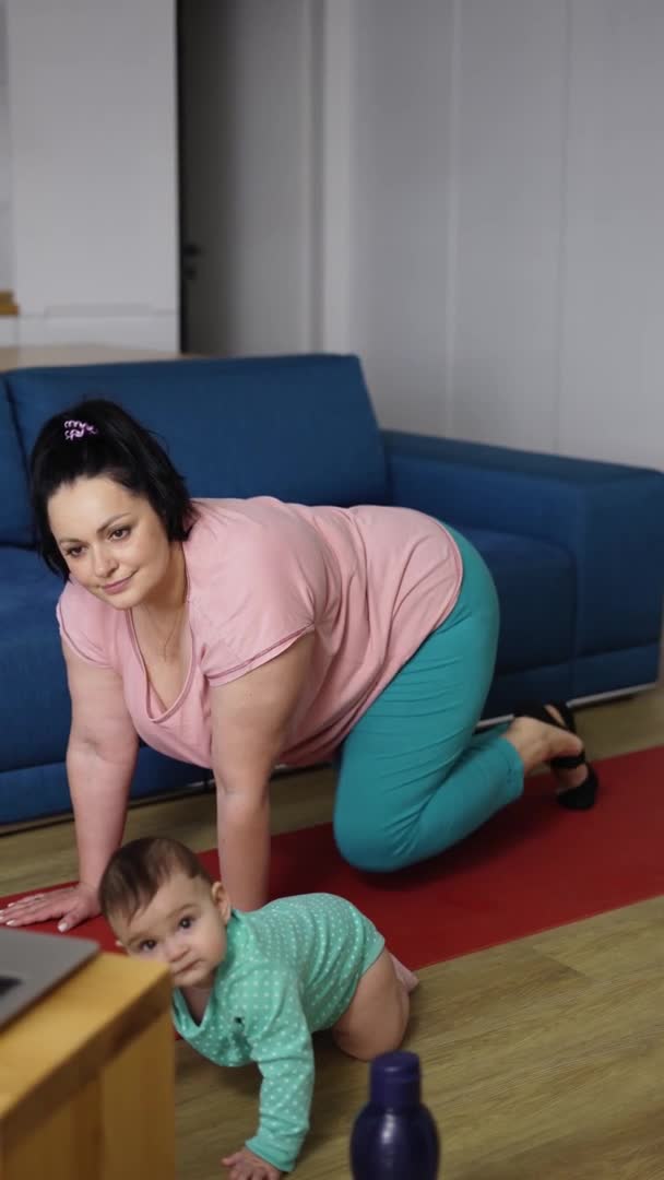 Заряджена жінка робить легені ніг онлайн з ноутбука з маленькою дитиною поруч з нею, повільний рух — стокове відео