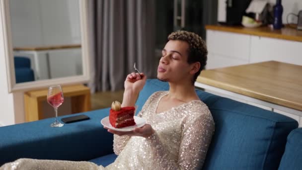 Un hombre en un vestido sentado en un sofá, admira un pedazo de pastel — Vídeo de stock