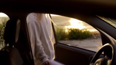 Sarışın kadın altın saatinde arabaya biniyor ve sahilde arabayı çalıştırıyor.