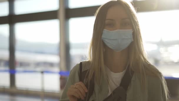 Retrato de una hermosa mujer rubia feliz con una máscara protectora en el aeropuerto — Vídeos de Stock