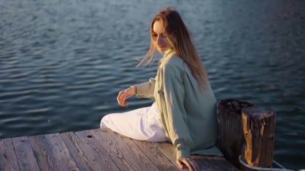 Imágenes de cerca de una chica feliz sentada en un muelle de madera — Vídeo de stock