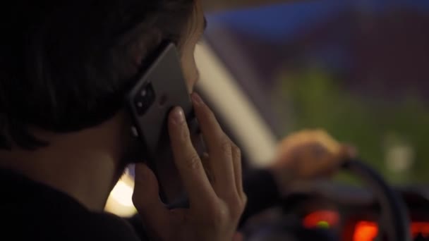 Pandangan samping dari seorang pria berbicara melalui telepon selama mengemudi di kota malam — Stok Video