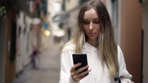 Mujer rubia caminando por la calle vieja usando teléfono inteligente — Vídeos de Stock